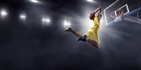 Fotobehang Basketball player makes slam dunk on big professional arena. Player flies through the air with the ball. Player wears unbranded clothes. © Alex