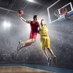 Basketball player makes slam dunk on big professional arena. Player flies through the air with the ball. Opponents try to prevent the ball from hitting the basketball ring.