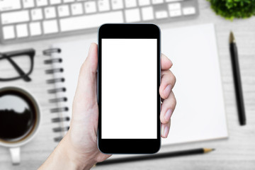 Hand holding smartphone with white blank screen over wood desk table.