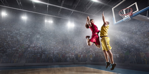 Fototapeta na wymiar Basketball player makes slam dunk on big professional arena. Player flies through the air with the ball. Opponents try to prevent the ball from hitting the basketball ring.
