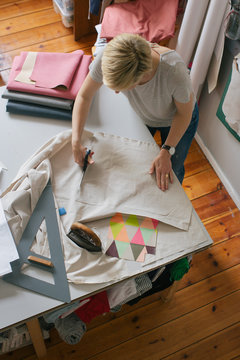 Overhead Shot of Blond Female Designer Cutting Fabric in Bright Dressmaking Workshop