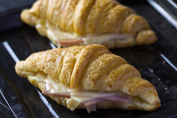 Newly baked butter croissant with ham and cheese sandwiches on old black baking tray - Powered by Adobe