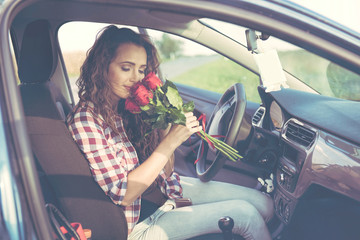 A beautiful young woman is sitting in the car and holding a bouquet of roses in her hand