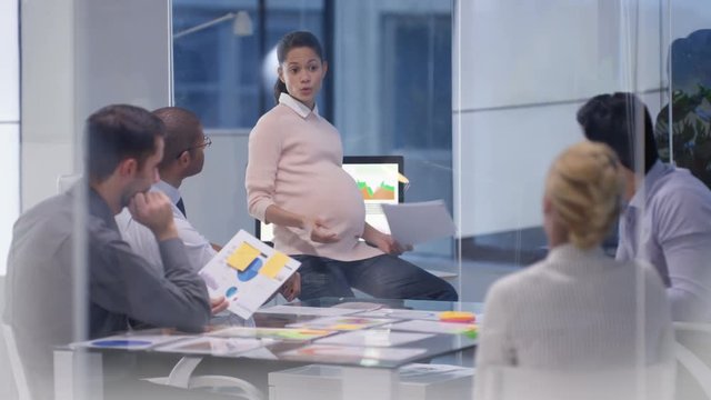  Pregnant businesswoman in a meeting with colleagues discussing financial data