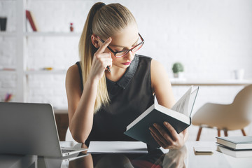 Attractive woman reading book in office - Powered by Adobe