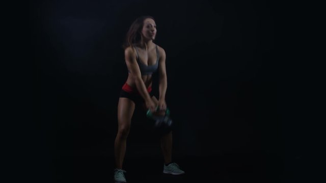  Fit young woman working out with kettle bell weight against black background