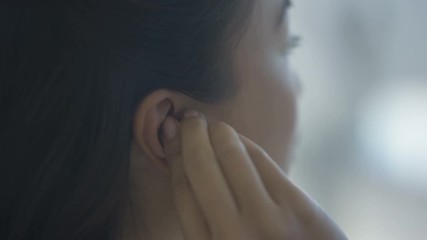  Close up of young Asian woman putting a hearing aid into her ear
