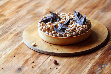 Pear Tart with Hazelnuts,  Milk Chocolate Cream and Streusel Topping decorated with chocolate leaves, on wooden board, on wooden background.