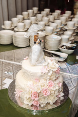 a multilevel white wedding cake with pink flowers and figurines