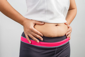 Overweight woman hand pinching excessive belly fat on gray background, Healthy concept 