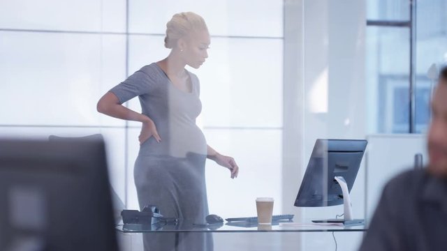  Pregnant businesswoman standing to work at her desk in modern office