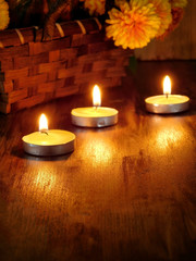 Lighted candles and a wicker basket with a pumpkin and flowers in the background