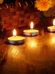 Lighted candles and a wicker basket with a pumpkin and flowers in the background
