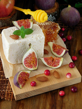 Cheese made of sheep milk and slices of figs on a wooden board surrounded by cranberries and almond. Ingredients for a cheese plate