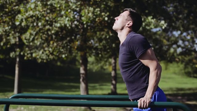 Fit man doing triceps dips on parallel bars at park exercising outdoors