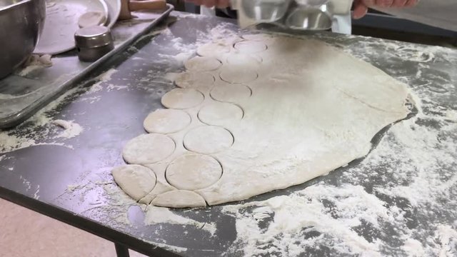 A man rolls a cutter to make round dough circles in preparation for making pierogies.  	