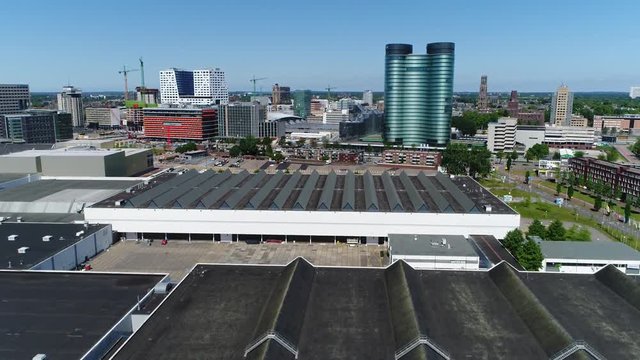 Urban aerial of modern city center of Utrecht showing modern glass building and in further background showing Dom Tower on right and central train station of Utrecht on left side blue sky background
