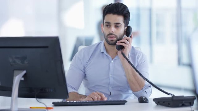  Cheerful Asian businessman making phone call at his desk in modern office