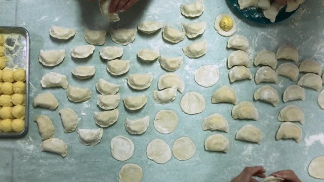 A unique bird's eye view of women pinching and making potato-filled pierogies.  	