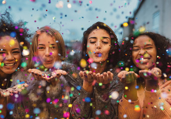 Fototapeta Young women blowing confetti from hands. Friends celebrating outdoors in evening at a terrace. obraz