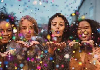 Foto op Plexiglas Young women blowing confetti from hands. Friends celebrating outdoors in evening at a terrace. © Artem Varnitsin