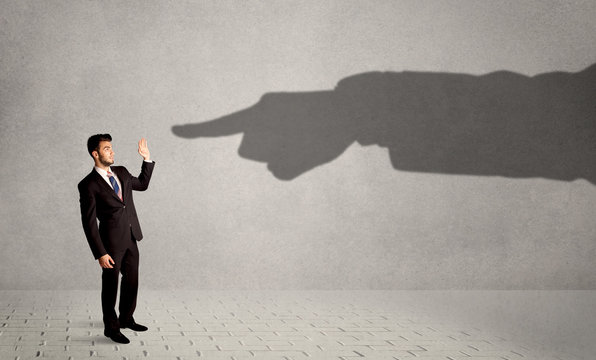 Business person looking at huge shadow hand pointing at him concept