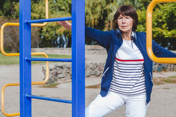 Fototapeta na wymiar elderly woman performs squatting on summer sports ground