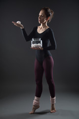 Obraz premium A young slim dancer holds sweet in a dark room after her dance class. Concept idea of a bad habit to be addicted to sweet, sugar. A decision making point - what to choose to make sport or to eat sweet