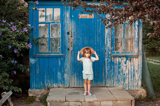 Dilapidated porch of an old house. Little girl standing on the stairs, and playing with his hat.