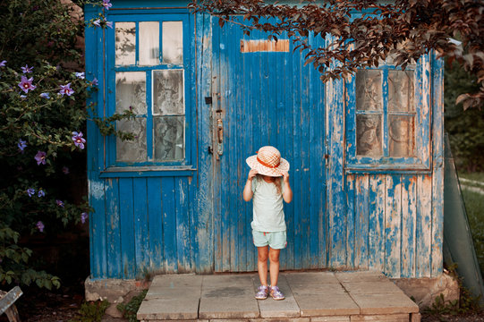 Dilapidated porch of an old house. Little girl standing on the stairs, and covers his face with a hat.