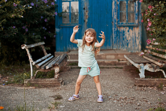 Dilapidated porch of an old house. Two old bench near the porch. Little girl dancing.