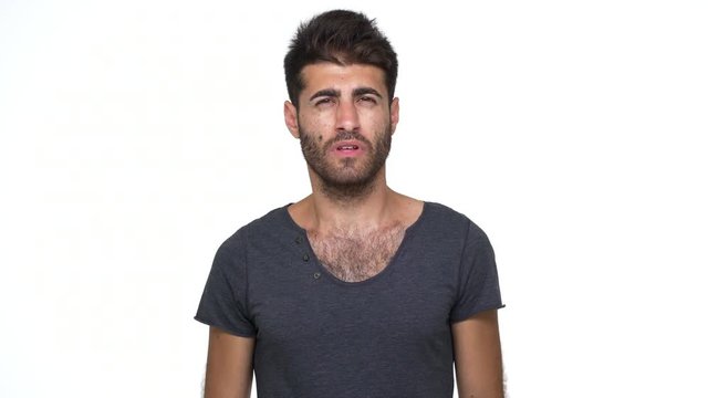 caucasian young man wearing grey t-shirt looking at camera expressing misunderstanding throwing up hands saying "what" over white background. Concept of emotions