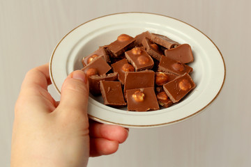 Female hand holding a plate with broken chocolate with nuts