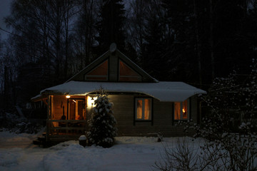 A country house in the evening twilight in the winter. The windows shine warm light