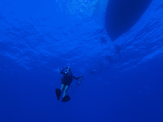 Diver Descending into the Blue Ocean below Boat Silhouette on Surface