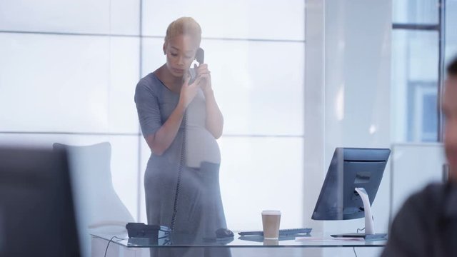  Pregnant businesswoman making phone call at her desk in modern office