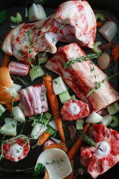 Beef and ox bones in an oven tray with vegetables and thyme.