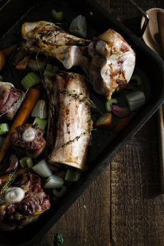Crop view of a tray of roasted oxtail and beef bones with vegetables.
