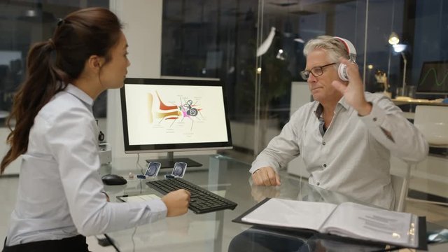  Mature man wearing headphones, getting a hearing test with audiology doctor. 