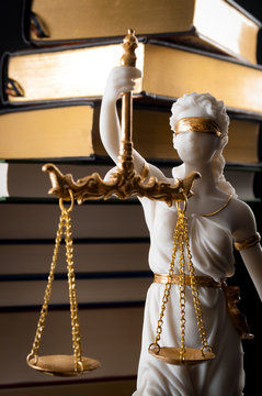 Legal code, enforcement of the law and blind Iustitia concept with statue of the blindfolded lady justice ( Dike in Greek and Justitia in Roman mythology), and a stack of books