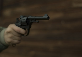 A revolver with a cocked trigger in hand is aiming past the frame against the background of a...