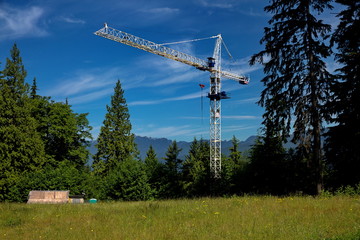 Obraz premium Place for future construction site on Burnaby Mount, a construction crane on a place covered with green grass against the background of a forest and a mountain ridge