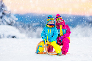 Children play in snow on sleigh in winter park