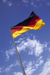 German flag on flagpole flapping in the wind in front of a blue sky