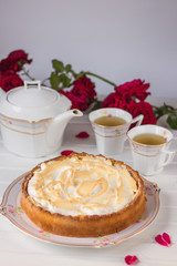 Meringue pie on a white table near teapot and cups and red roses.