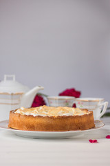 Meringue pie on a white table near teapot and cups and red roses.
