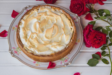 Meringue pie on a white table near red roses.