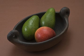 Avocados and apple in an archaic clay bowl