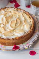 Meringue pie on a white table near red roses and cups with tea.