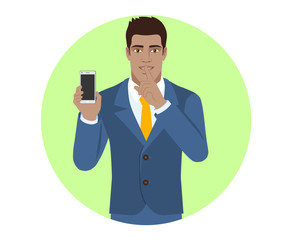 Hush hush. Businessman holding mobile phone and shows hush-hush sign